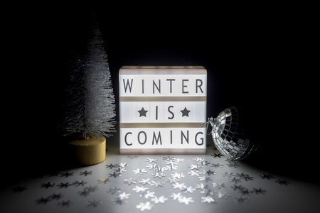 Still life with a silver Christmas tree, a disco ball and a lightbox with the inscription Winter is coming.の写真素材