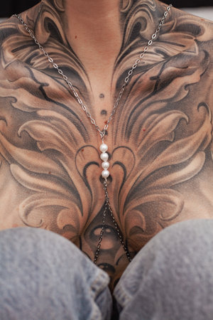 A close-up view of a persons chest area revealing an ornate tattoo adorned with a silver chain and pearl necklace.の写真素材