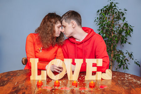 A man and woman are seated at a table, facing each other, in front of a brightly lit, Love sign.の写真素材