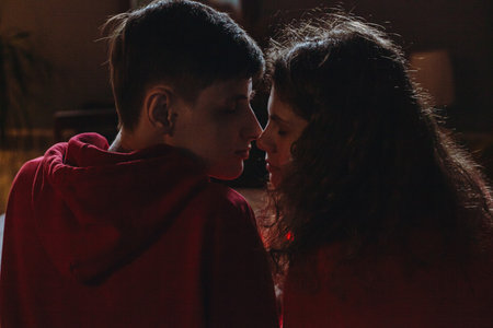 A young couple gazes into each others eyes, sharing a close, intimate moment in the soft glow of...