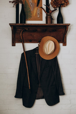 A vintage coat hangs neatly on a wooden shelf decorated with a rustic hat and a stylish cane. The warm tones create a cozy atmosphere in the inviting living space.の写真素材