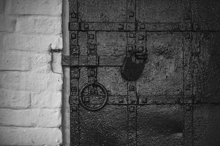 Old black iron door with padlock and ring in rustic building setting