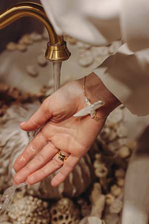 A young woman washes her hands under a flowing faucet, adorned with unusual pearl beads. The...