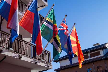 Colorful flags from multiple nations are proudly flying in the wind outside a cultural building on a sunny day. The scene showcases international diversity and unity.の写真素材