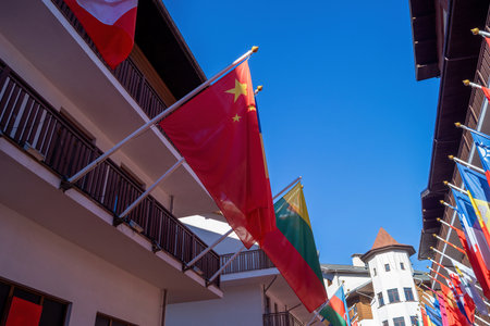 Brightly colored flags from various countries are fluttering in the wind against a clear blue sky. The scene features a beautiful building with balconies, enhancing the festive atmosphere.の写真素材