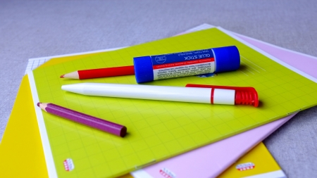 Two colored pencils, a pen and a glue-stick lying on a heap of copy-books