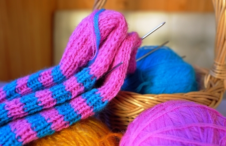 Blue woollen ball lying in a small basket with pink and yellow balls, knitting needles and half-knitted sock in front of itの写真素材