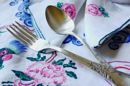 Table-cloth and table-napkins with embroidered parrot, flowers and decorative ornament with a spoon and a fork lying on itの写真素材