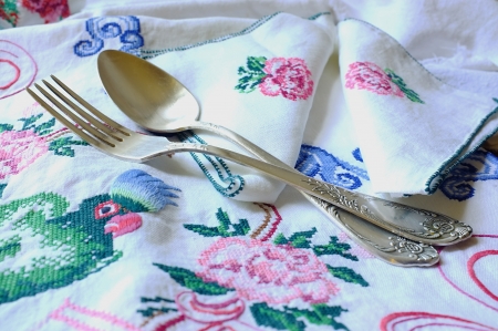 Table-cloth and table-napkins with embroidered parrot, flowers and decorative ornament with a spoon and a fork lying on itの写真素材