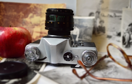An old camera lying on its back, an apple   glasses on the background of old photosの写真素材