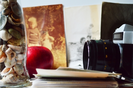 A stilllife with old camera, old photos, a fresh apple and a glass bottle with shells and stonesの写真素材