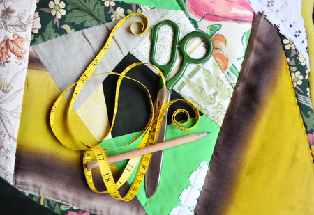 Tape-measure, scissors and pencil lying on a patchworky chair cushion handmade with  crazy patch ...