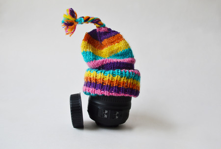 Lens wearing a bobble knitted striped hat against condensation and a lens cap near itの写真素材
