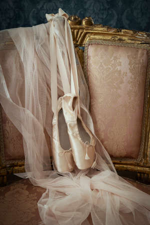 A pair of pink satin pointe ballet shoes on a vintage chair with tulle fabric