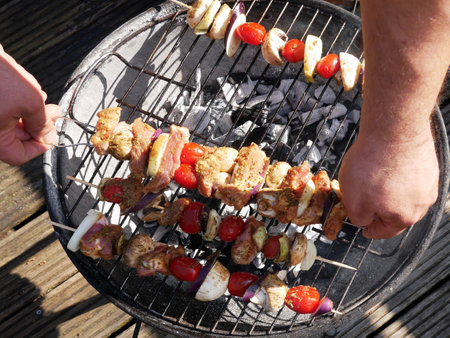 The hands of a man who is arranging colorful and tasty skewers on the hearth of a barbecue.の写真素材