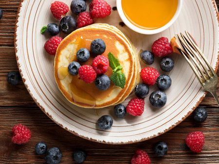 Pancakes with berries and honey on wooden table, top view. Sweet breakfast or brunch meal.の写真素材