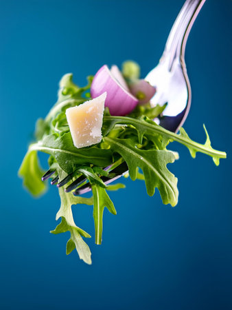 A close-up of a fork with a vibrant salad, contrasted with a striking blue background, emphasizing the freshness. Parmesan shavings, shallots and arugula.の写真素材