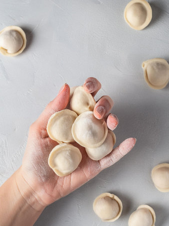 A woman's flour-covered hand holding tiny pelmeni dumplings just before they are cooked.の写真素材