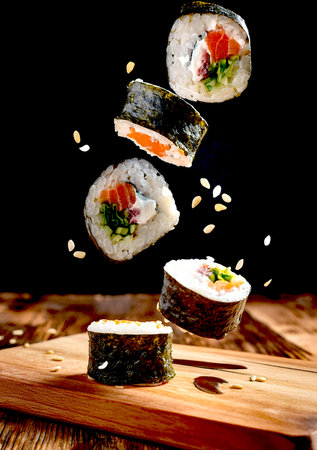 A beautifully arranged platter of sushi displayed on a rustic wooden cutting board, showing vibrant colors and textures. Flying food concept.の写真素材