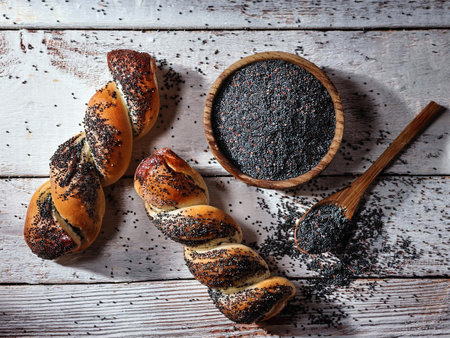 Twisted poppy seed bread rolls on rustic wooden table with a bowl and spoon filled with poppy seeds,...