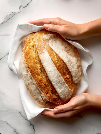A person gently holds a freshly baked loaf of bread on a white surface, highlighting its artisanal quality and inviting appearance.の写真素材