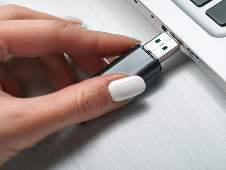 A person presents a USB drive near a laptop, suggesting the act of saving or transferring digital information.の写真素材
