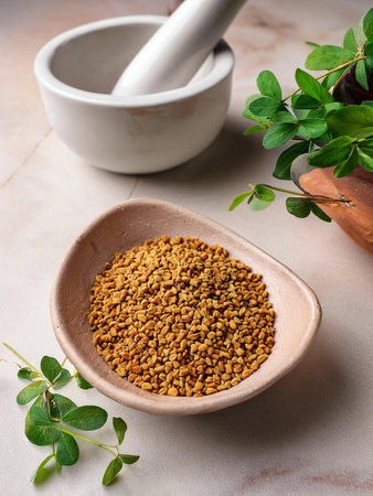 Fenugreek seeds in a ceramic bowl on a marble surface, surrounded by fresh green fenugreek leaves. White mortar in the background.の写真素材