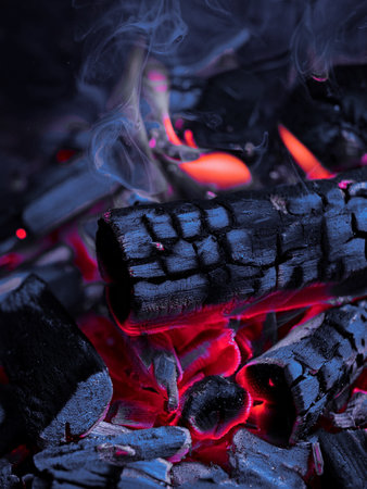 Close-up of glowing red embers and charred wood logs in a fireplace, showing the intense heat and vibrant colors of burning coals. Ideal image for themes related to warmth, fireの写真素材