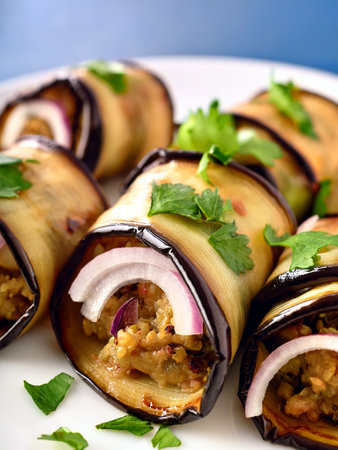Georgian eggplant rolls (nigvziani badrijani) filled with walnuts, garlic and spices, garnished with fresh cilantro and pickled red onions on a white plate. Close-up.の写真素材