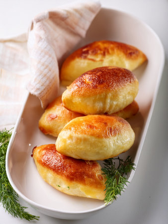 A plate with four freshly baked potato piroshki with bacon and cheese, in white tones, with fresh dill, golden brown and inviting, ready to serve.の写真素材