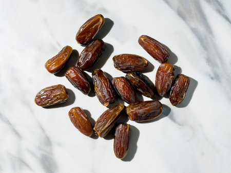 Fresh dates displayed on a polished white marble surface, showing their natural texture and deep brown hue.の写真素材