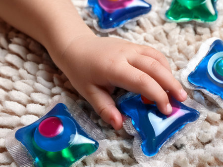 Child's hand touching colorful laundry detergent pods on a textured surface. Danger, risk of poisoning.の写真素材