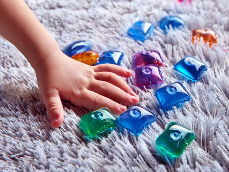 Child's hand touching colorful laundry detergent pods on a textured surface. Danger, risk of poisoning.の写真素材