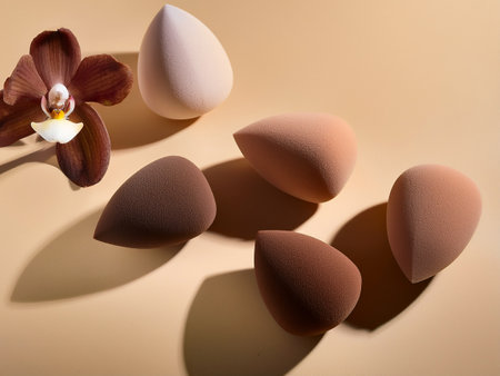A set of makeup sponges in various colors alongside a fresh orchid, highlighting beauty and floral elegance.の写真素材