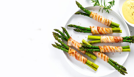 Bacon-wrapped asparagus spears arranged on a white plate with a side of creamy dipping sauce, perfect for a healthy appetizer or keto snack.の写真素材