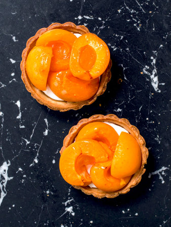 Mini apricot tarts with fresh fruit topping on a black marble background, delicious pastry dessert.の写真素材