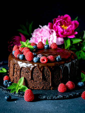 Luxurious chocolate cake garnished with assorted berries and mint, presented on a contrasting black backdrop.の写真素材