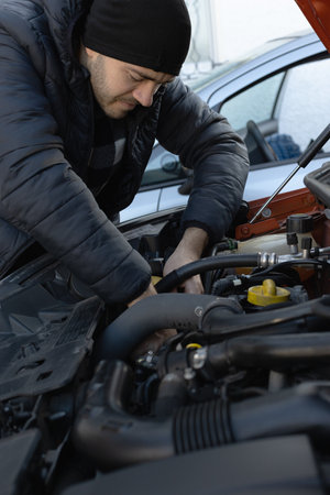 Mans Hands Using Tools to Repair a Car Engine Beneath the Open Hood, Mechanical Expertise in Automotive Maintenanceの写真素材