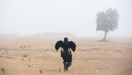 woman wearing blackangel wings walks into a fogの写真素材