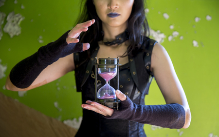 hands of a woman dressed in dark, holding an hour clock with time running outの写真素材