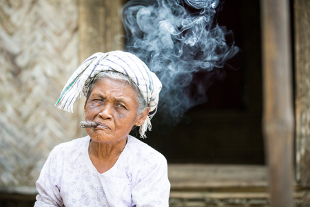 CHITTAGONG, BANGLADESH - CIRCA FEBRUARY 2016: old lady smoking a cigar at her porch with smoke raising above herのeditorial素材