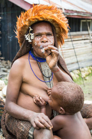 Baliem Valley, West Papua, Indonesia, February 2016: dani tribe woman smoking while breastfeeding her babyのeditorial素材