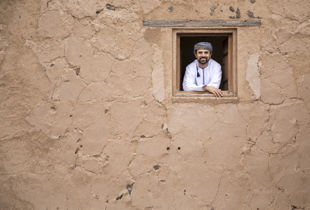 Arab man in traditional Omani outfit looking out of a windowの写真素材