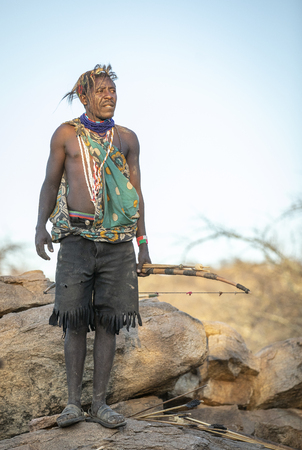 Lake Eyasi, Tanzania, 11th September 2019: Hadzabe man on a rock with his bow and arrowsのeditorial素材