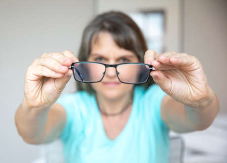 middle aged woman traying to fix her glasses to see betterの写真素材