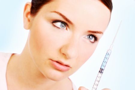 A pretty woman looking at the needle of a syringe. Focus is on the needle.の写真素材