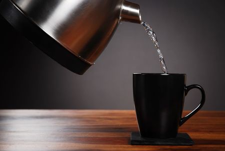 Kettle pouring water into mug on dark backgroundの写真素材