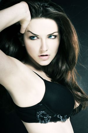 A young brunette posing in a bra in front of a dark background.の写真素材