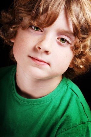 A cute young boy looking to the camera on a black background.の写真素材