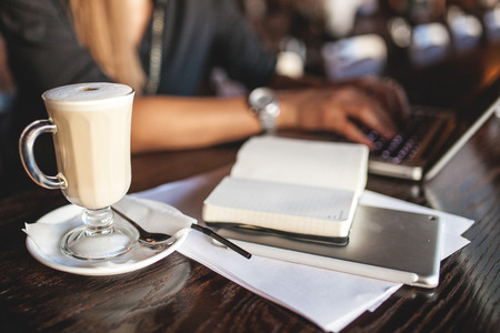 Business woman in glasses indoor with coffee and laptop taking notes in restaurantの写真素材